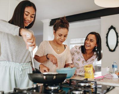 Three girls making food together standing in kitchen